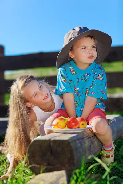 Милая блондинка и мальчик в смешной шляпе играют с фруктами — стоковое фото
