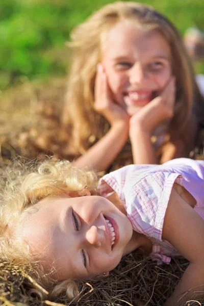Милая маленькая девочка с светлыми волосами, валяющаяся в куче сена по зеленому закону — стоковое фото