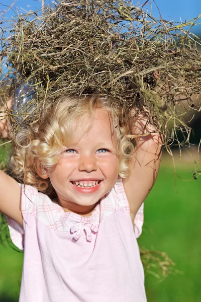 Милая маленькая девочка с кудрявыми светлыми волосами, играющая с кучей сена — стоковое фото