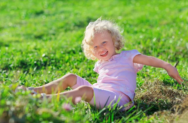 Roztomilá holčička s blond kudrnaté vlasy hraje jn zelený trávník vtipu — Stock fotografie