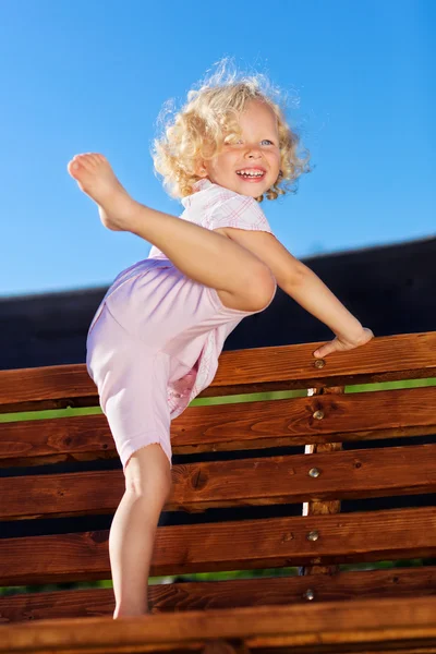 Linda niña con el pelo rubio rizado jugando en la cadena de madera s —  Fotos de Stock