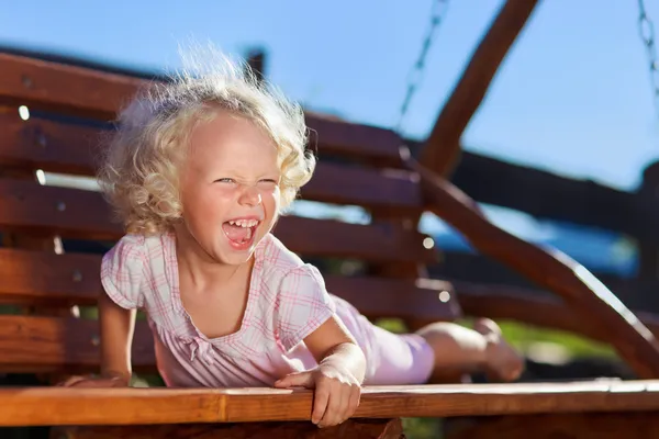 Cute little girl with blond curly hair playing on wooden chain s — Stock Photo, Image