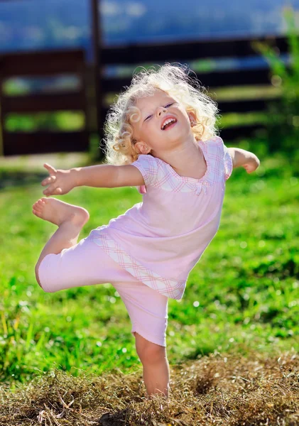 Petite fille mignonne avec des cheveux bouclés blonds jouant sur la pelouse verte avec — Photo