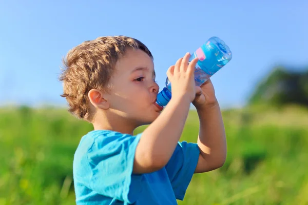 Little boy drinking gas water on green grass field — Stock Photo, Image