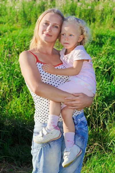 Beautiful mother with infant curly-headed blond daughter on mead — Stock Photo, Image