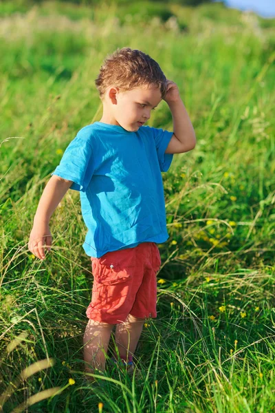 Menino pensando duro em pé no gramado de grama verde — Fotografia de Stock