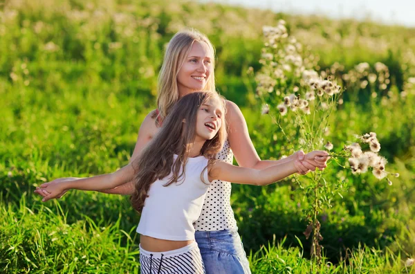Beautiful mother and daughter family playing on meadow in sunset — Stock Photo, Image