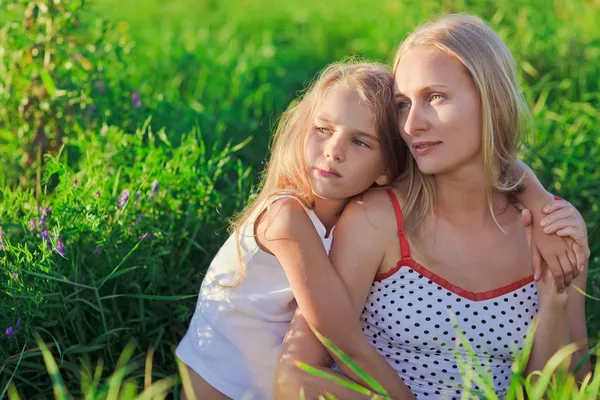 Beautiful mother and daughter sitting on green lush grass meadow — Stock Photo, Image