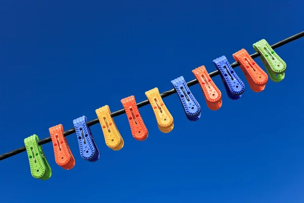 Line of multicolor plastic clothes pegs hanging in front blue sk — Stock Photo, Image