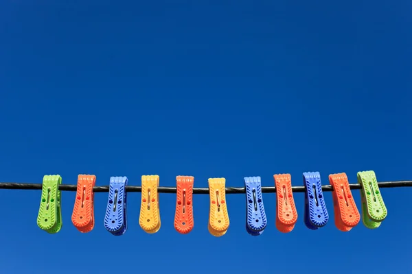 Лінія різнокольорового пластикового одягу кілочки висять у передній блакитній шкірі — стокове фото