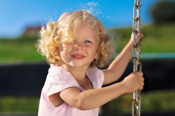 Cute little girl with blond curly hair playing on wooden chain s — Stock Photo, Image