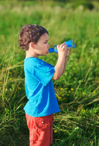 Мальчик пьет газовую воду на зеленой траве — стоковое фото