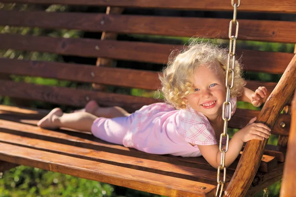 Милая маленькая девочка с кудрявыми светлыми волосами, играющая на деревянных цепях — стоковое фото