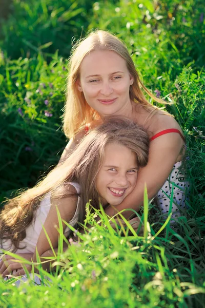 Прекрасные мать и дочь сидят на зеленом лугу пышной травы — стоковое фото