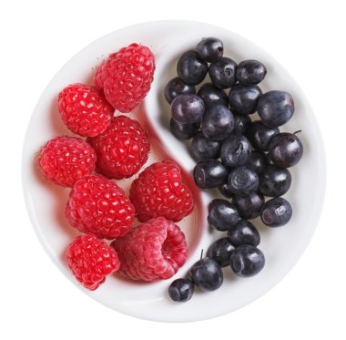 Red raspberry versus black bilberry in Yang Yin shaped plate, is clipart