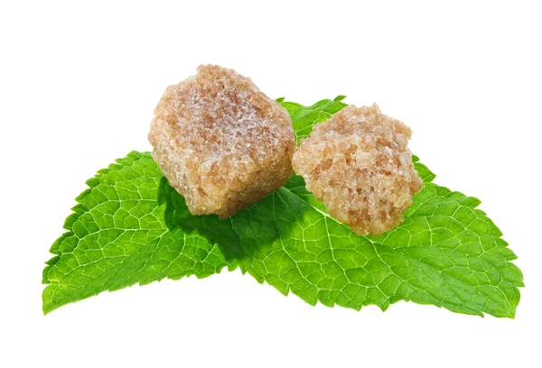 Dois cubos de açúcar de cana-de-açúcar marrom sobre folhas de hortelã-pimenta, isolados — Fotografia de Stock