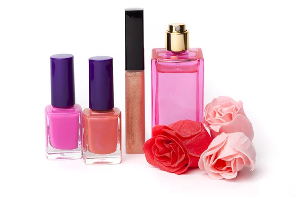 Labbra lucide, profumo, bottiglie di smalto e fiori di rosa su sfondo bianco Immagine Stock