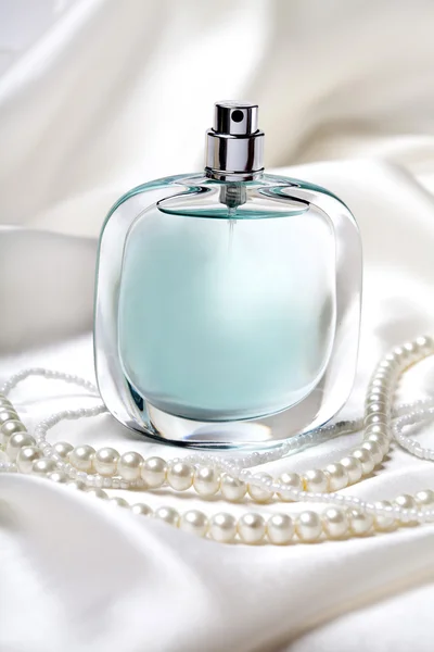 Frasco de perfume azul y collar de perlas en el fondo de seda blanco —  Fotos de Stock