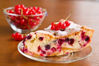 Piece of berry pie on saucer and red currants in bowl