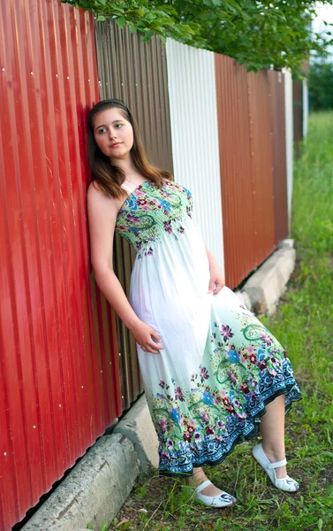 Dívka v lehké šaty proti kovový plot — Stock fotografie