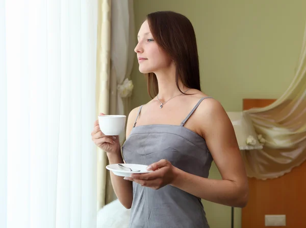 Jovem mulher bebendo chá perto da janela — Fotografia de Stock