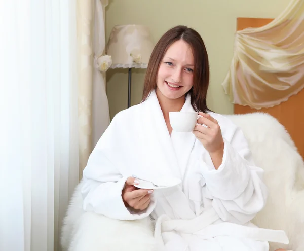 Молода жінка в білому халаті п'є чай — стокове фото