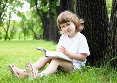 küçük kız parkta bir kitap okuma portresi