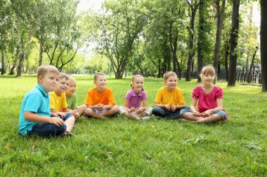 Group of children sitting together in the park clipart