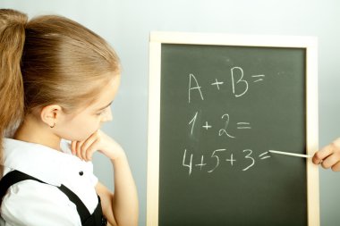 School girl looking at the blackboard with exercises and thinkin clipart