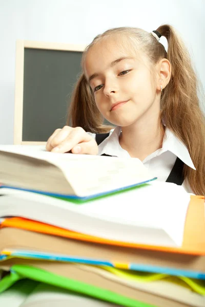 Chica de la escuela haciendo tarea detrás de pila de libros . —  Fotos de Stock