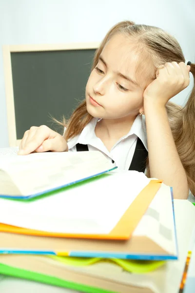 Schulmädchen macht Hausaufgaben hinter Bücherstapel. — Stockfoto