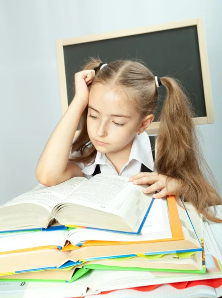 Chica de la escuela haciendo tarea detrás de pila de libros . —  Fotos de Stock