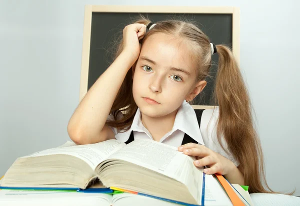 Chica de la escuela haciendo tarea detrás de pila de libros . — Foto de Stock
