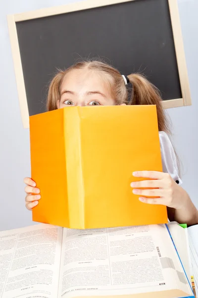 École fille se cachant derrière jaune livre — Photo