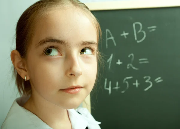 Schoolgirl thinking about exercises written on the blackboard — Stock Photo, Image