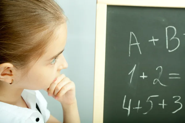 School girl looking at the blackboard with exercises and thinkin — Stock Photo, Image