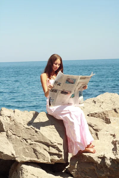 Girl reads newspaper near sea