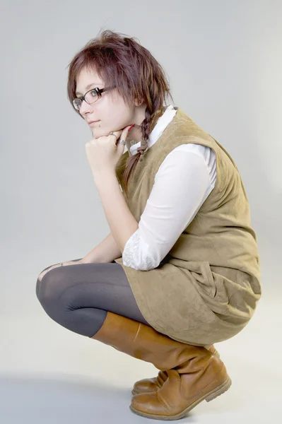 A girl sits on his haunches in a suede dress and leather boots. — Stock Photo, Image