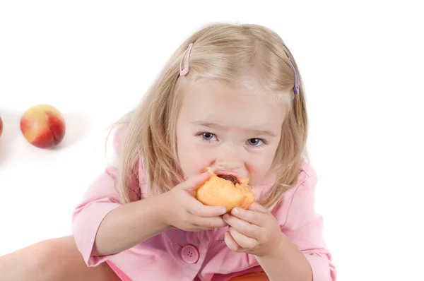 Little girl eating peach in studio — Stock Photo, Image