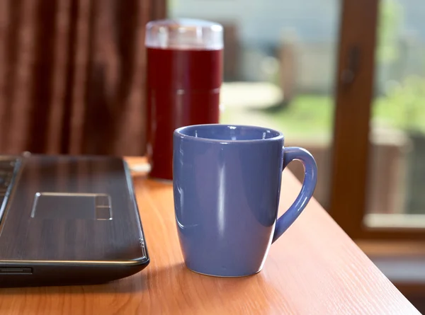 O amolador de café de computador portátil e xícara em uma mesa — Fotografia de Stock