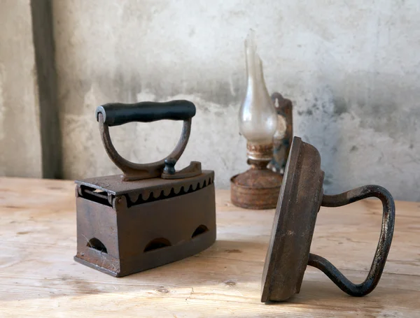 Oude strijkijzers en olie lamp op tafel — Stockfoto