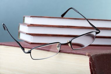 Glasses hang down from a pile of books clipart