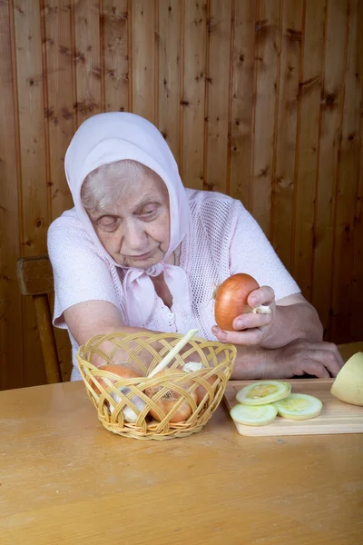Стара жінка торкається цибулі, сидячи — стокове фото