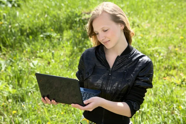 Menina-adolescente com o computador portátil contra uma grama verde — Fotografia de Stock