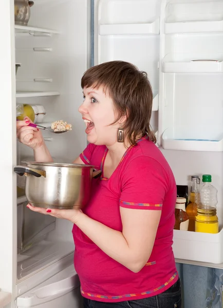 Γυναίκα που τρώει από το τηγάνι κοντά σε ψυγείο — Φωτογραφία Αρχείου