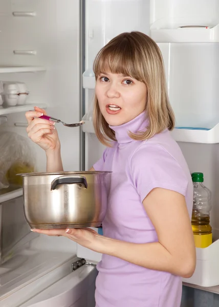 Frau isst aus Pfanne neben Kühlschrank — Stockfoto