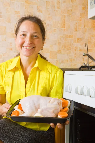 Женщина запихивает фаршированную курицу в духовку — стоковое фото