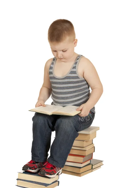 Kleiner Junge sitzt auf den Büchern und liest ein Buch — Stockfoto