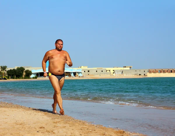 Людина з надмірною вагою біжить на пляжі — стокове фото