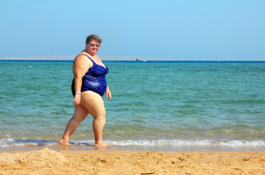 Overweight woman walking on beach clipart